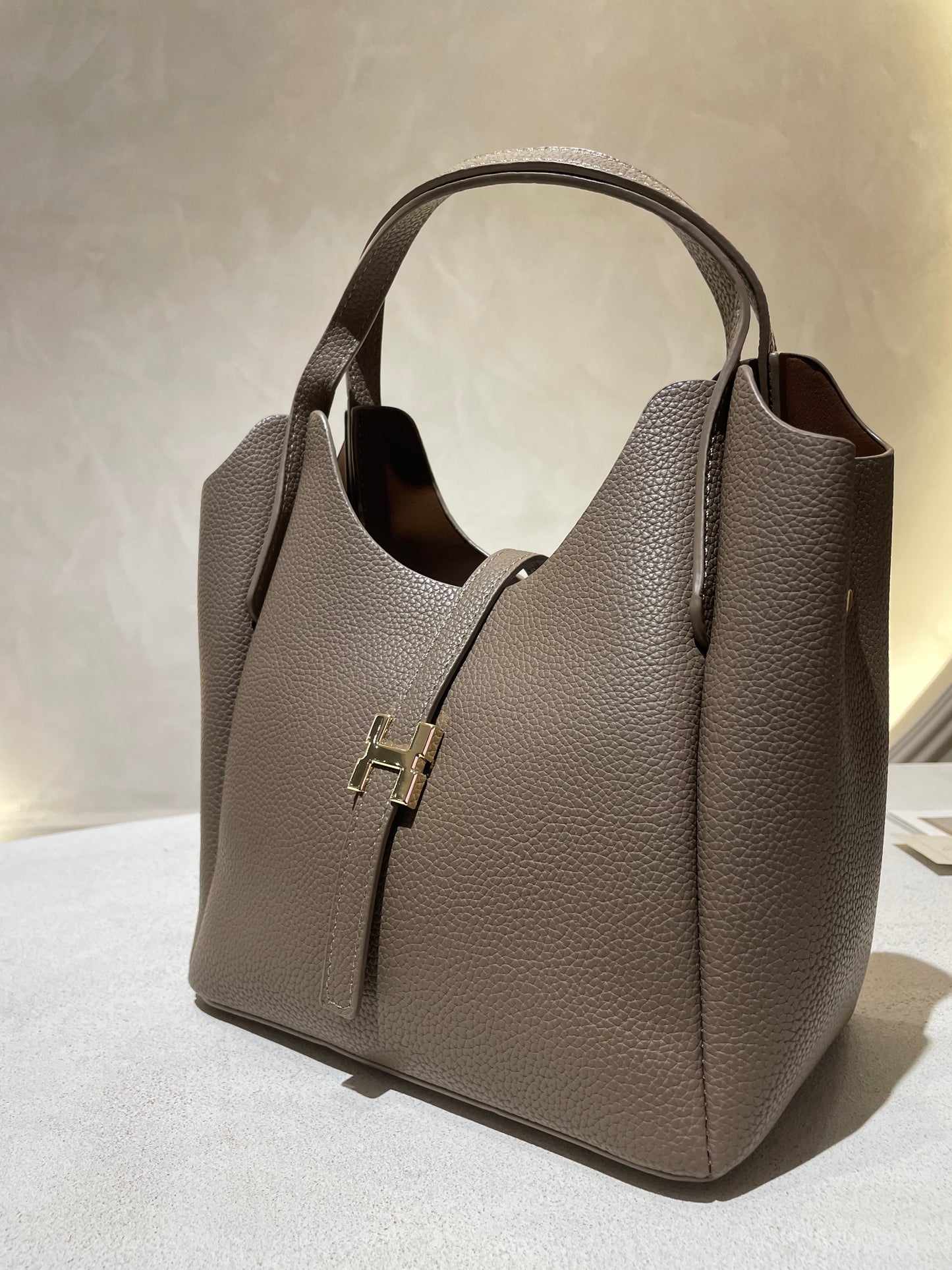 Découvrez le sac à main Hélia, une élégante pièce en simili cuir d'inspiration Hermès qui allie sophistication et raffinement. Disponible en cinq teintes raffinées — bordeaux, taupe, noir, camel et marron — ce sac se distingue par sa silhouette soignée et ses détails minutieux, notamment l’emblématique « H » en acier inoxydable doré. Avec une dimension idéale de 25 x 25 cm et une épaisseur de 14 cm, il offre un équilibre parfait entre style et fonctionnalité. Une bandoulière amovible complète ce modèle pour