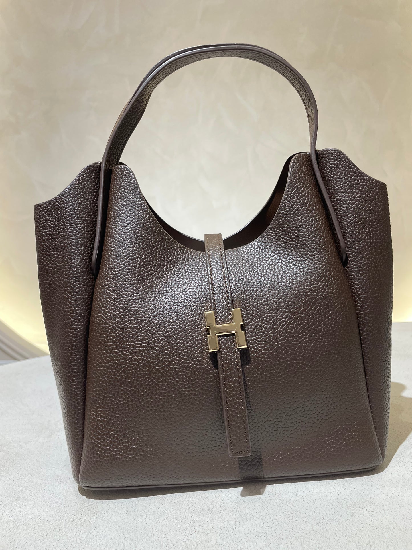 Découvrez le sac à main Hélia, une élégante pièce en simili cuir d'inspiration Hermès qui allie sophistication et raffinement. Disponible en cinq teintes raffinées — bordeaux, taupe, noir, camel et marron — ce sac se distingue par sa silhouette soignée et ses détails minutieux, notamment l’emblématique « H » en acier inoxydable doré. Avec une dimension idéale de 25 x 25 cm et une épaisseur de 14 cm, il offre un équilibre parfait entre style et fonctionnalité. Une bandoulière amovible complète ce modèle pour