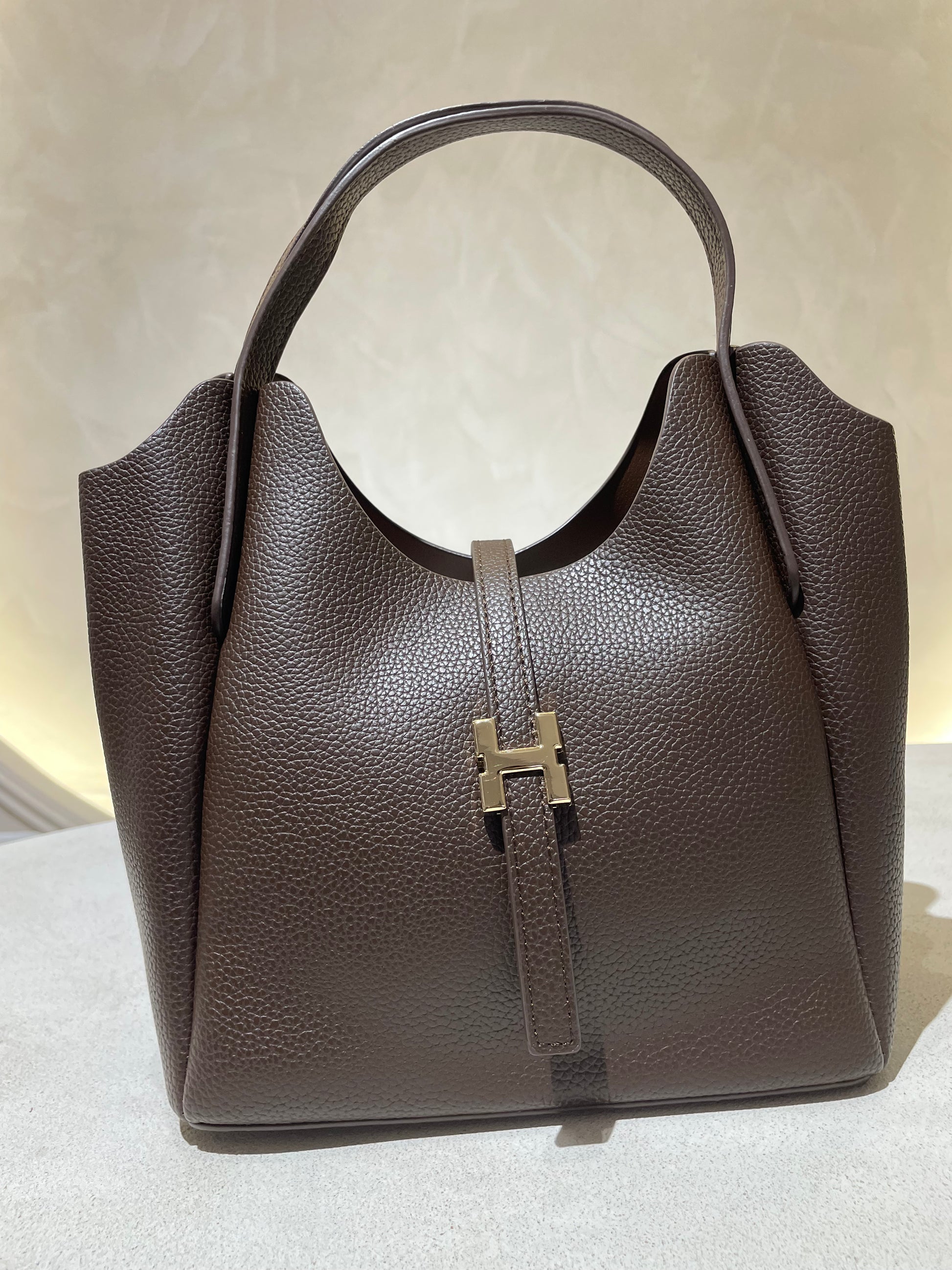 Découvrez le sac à main Hélia, une élégante pièce en simili cuir d'inspiration Hermès qui allie sophistication et raffinement. Disponible en cinq teintes raffinées — bordeaux, taupe, noir, camel et marron — ce sac se distingue par sa silhouette soignée et ses détails minutieux, notamment l’emblématique « H » en acier inoxydable doré. Avec une dimension idéale de 25 x 25 cm et une épaisseur de 14 cm, il offre un équilibre parfait entre style et fonctionnalité. Une bandoulière amovible complète ce modèle pour