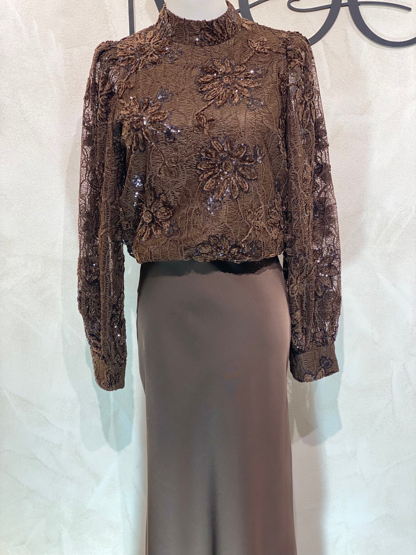 Le Haut Sandra allie élégance et modernité avec son col rond sophistiqué et sa délicate broderie en dentelle blanc nacré. Ses manches transparentes offrent une touche de légèreté, tandis que la finition impeccable garantit un look chic et raffiné. Idéal pour celles qui souhaitent se démarquer avec style et délicatesse.