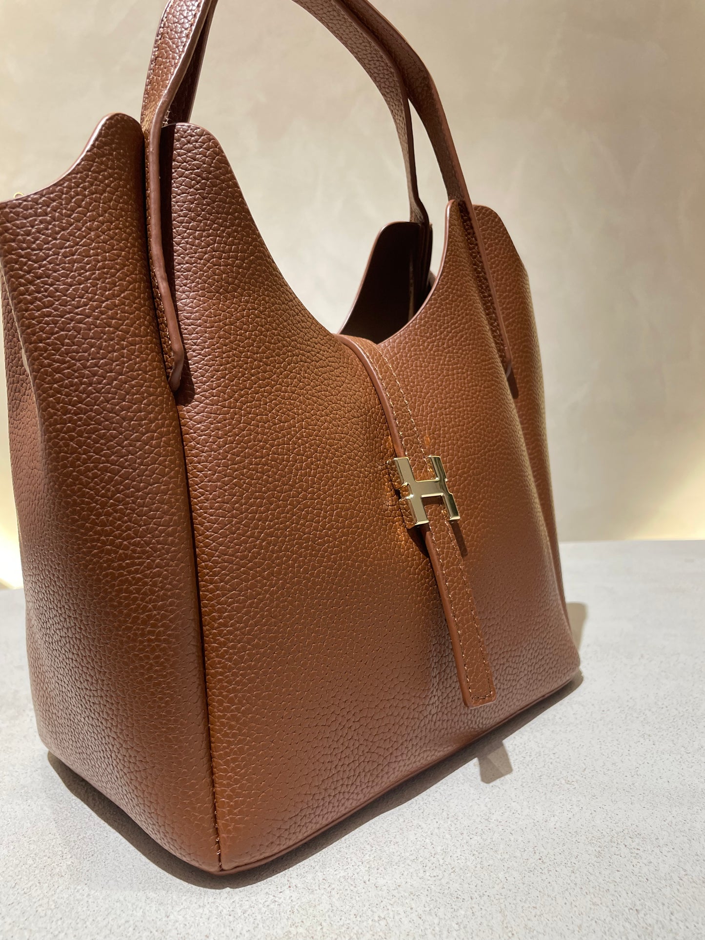 Découvrez le sac à main Hélia, une élégante pièce en simili cuir d'inspiration Hermès qui allie sophistication et raffinement. Disponible en cinq teintes raffinées — bordeaux, taupe, noir, camel et marron — ce sac se distingue par sa silhouette soignée et ses détails minutieux, notamment l’emblématique « H » en acier inoxydable doré , il offre un équilibre parfait entre style et fonctionnalité. Une bandoulière amovible complète ce modèle pour   