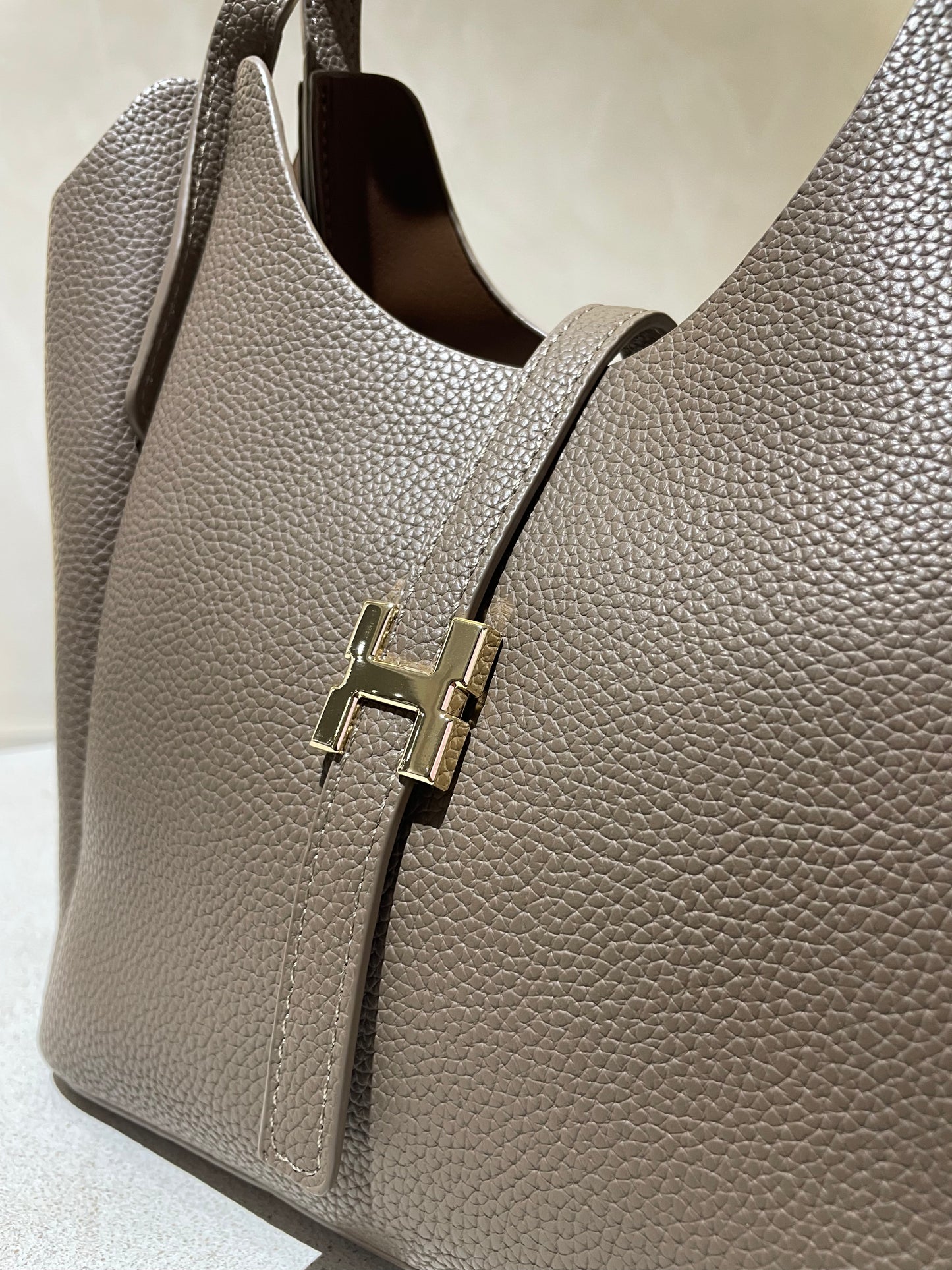 Découvrez le sac à main Hélia, une élégante pièce en simili cuir d'inspiration Hermès qui allie sophistication et raffinement. Disponible en cinq teintes raffinées — bordeaux, taupe, noir, camel et marron — ce sac se distingue par sa silhouette soignée et ses détails minutieux, notamment l’emblématique « H » en acier inoxydable doré. Avec une dimension idéale de 25 x 25 cm et une épaisseur de 14 cm, il offre un équilibre parfait entre style et fonctionnalité. Une bandoulière amovible complète ce modèle pour