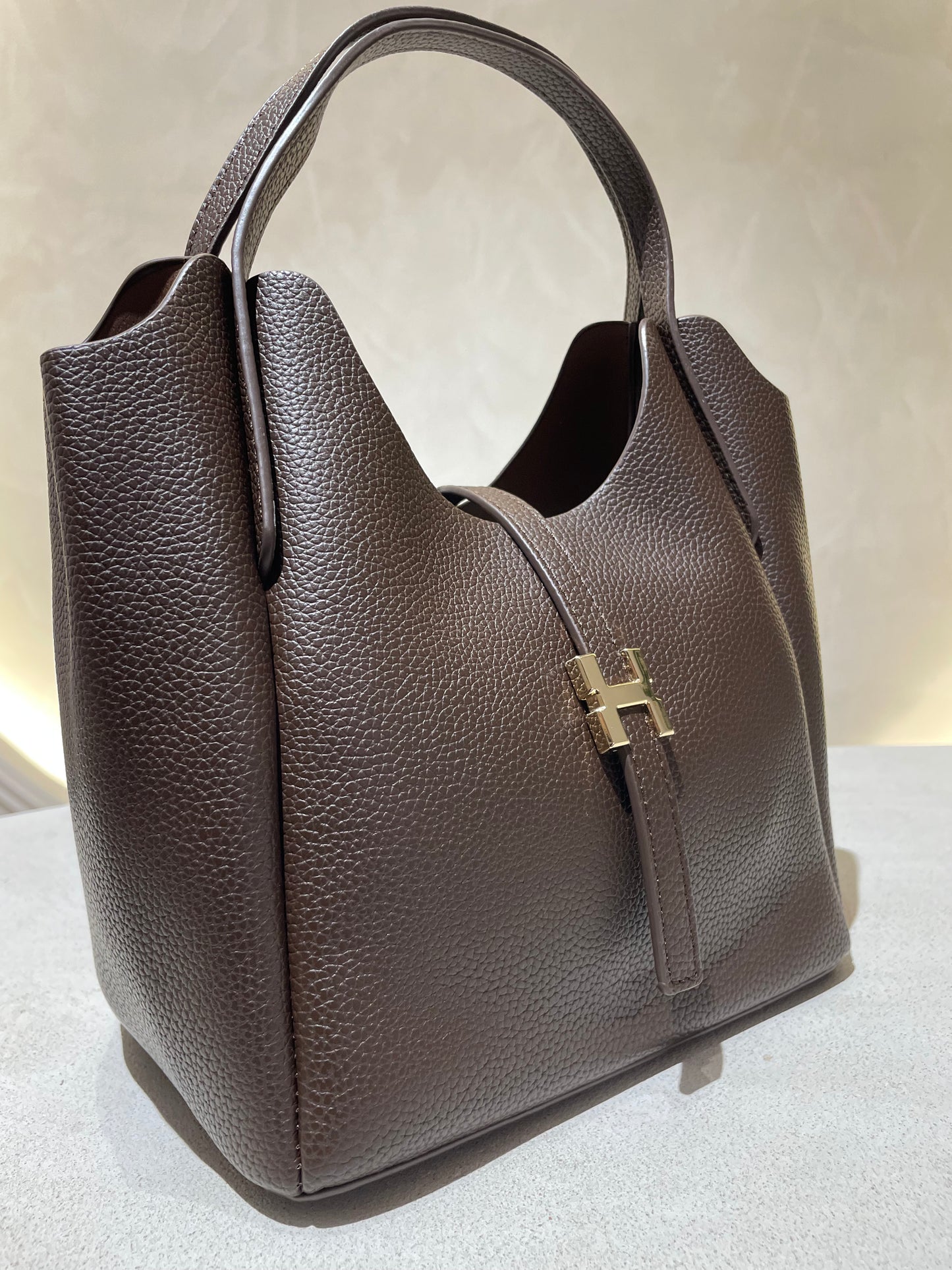 Découvrez le sac à main Hélia, une élégante pièce en simili cuir d'inspiration Hermès qui allie sophistication et raffinement. Disponible en cinq teintes raffinées — bordeaux, taupe, noir, camel et marron — ce sac se distingue par sa silhouette soignée et ses détails minutieux, notamment l’emblématique « H » en acier inoxydable doré. Avec une dimension idéale de 25 x 25 cm et une épaisseur de 14 cm, il offre un équilibre parfait entre style et fonctionnalité. Une bandoulière amovible complète ce modèle pour