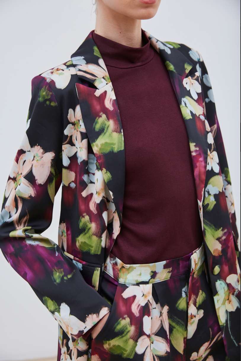 La veste Flora allie élégance et originalité avec ses motifs floraux abstraits aux nuances subtiles de beige, violet, bleu ciel et vert sur un fond noir profond. Sa coupe chic est sublimée par une ceinture et deux boutons délicats, apportant une touche raffinée et structurée. Parfaite pour affirmer un style sophistiqué tout en restant tendance.